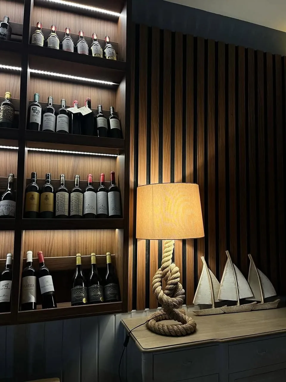 Garrafeira iluminada sobre painel ripado num restaurante
