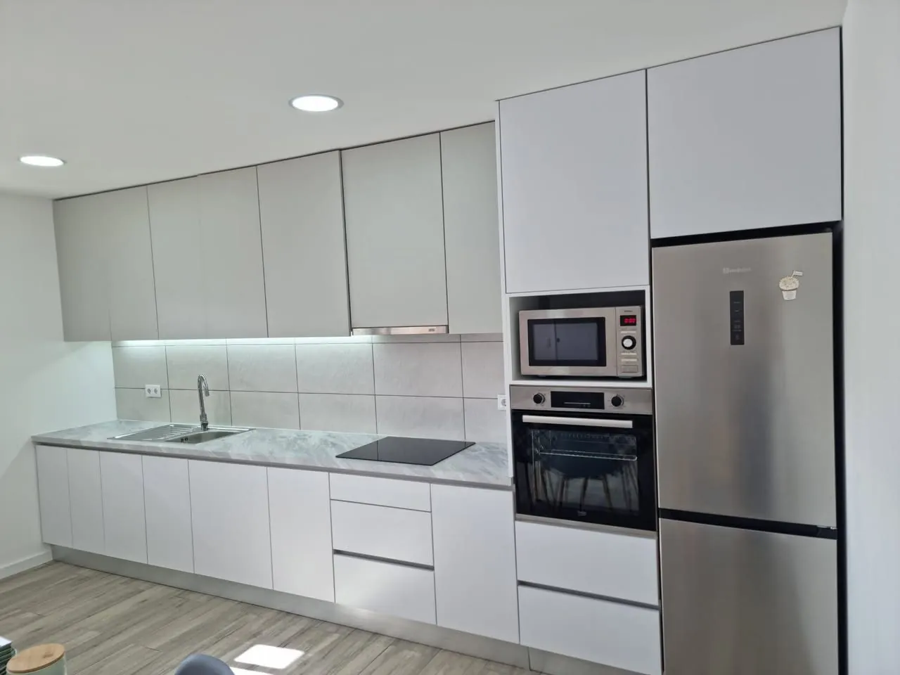 Cozinha branca com micro-ondas encastrado e frigorífico