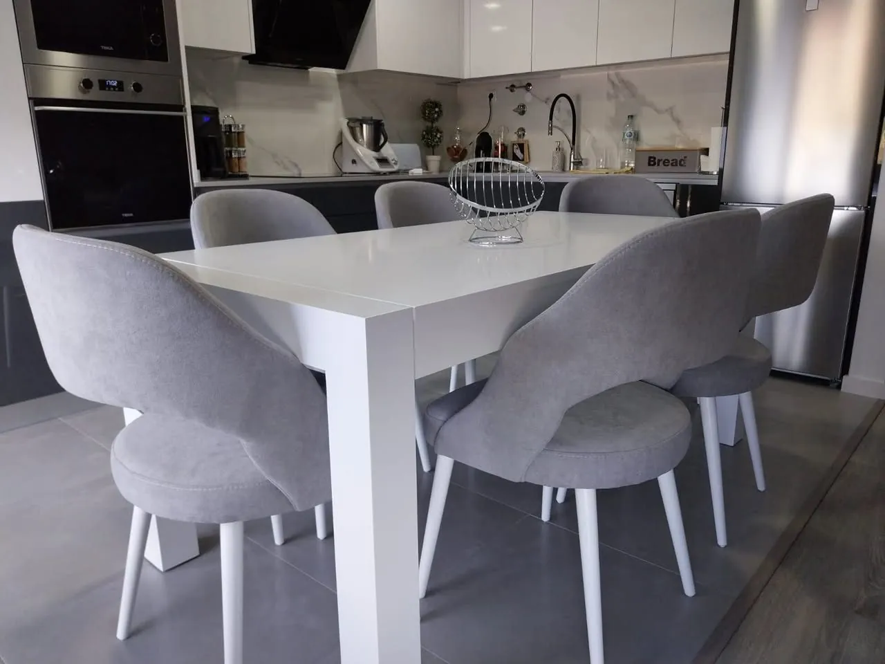 Mesa de jantar branca com cadeiras junto à cozinha